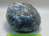 A smooth, shiney or scaly, naturally polished, mostly blue piece of serpentinite, tapered on both ends like a watermelon seed.